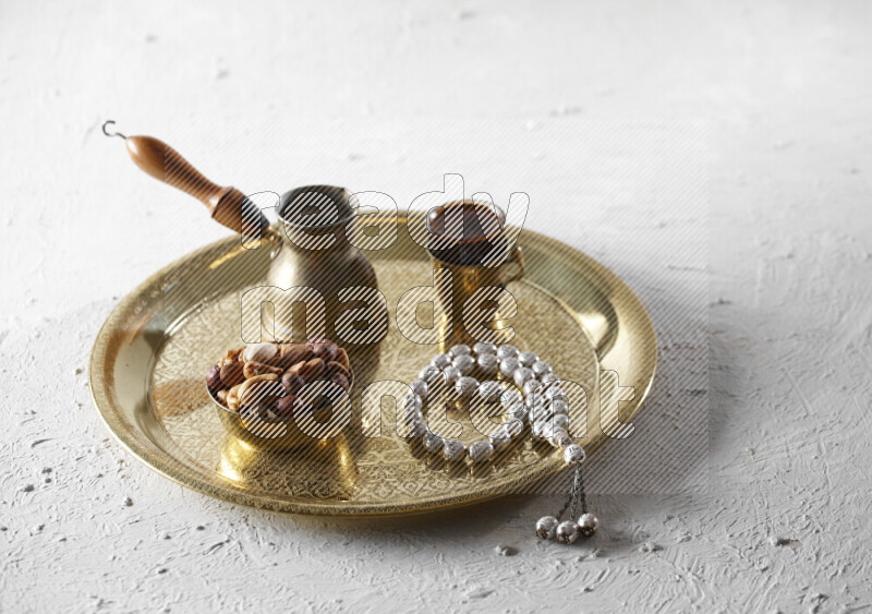 Nuts in a metal bowl with coffee and prayer beads on a tray in a light setup