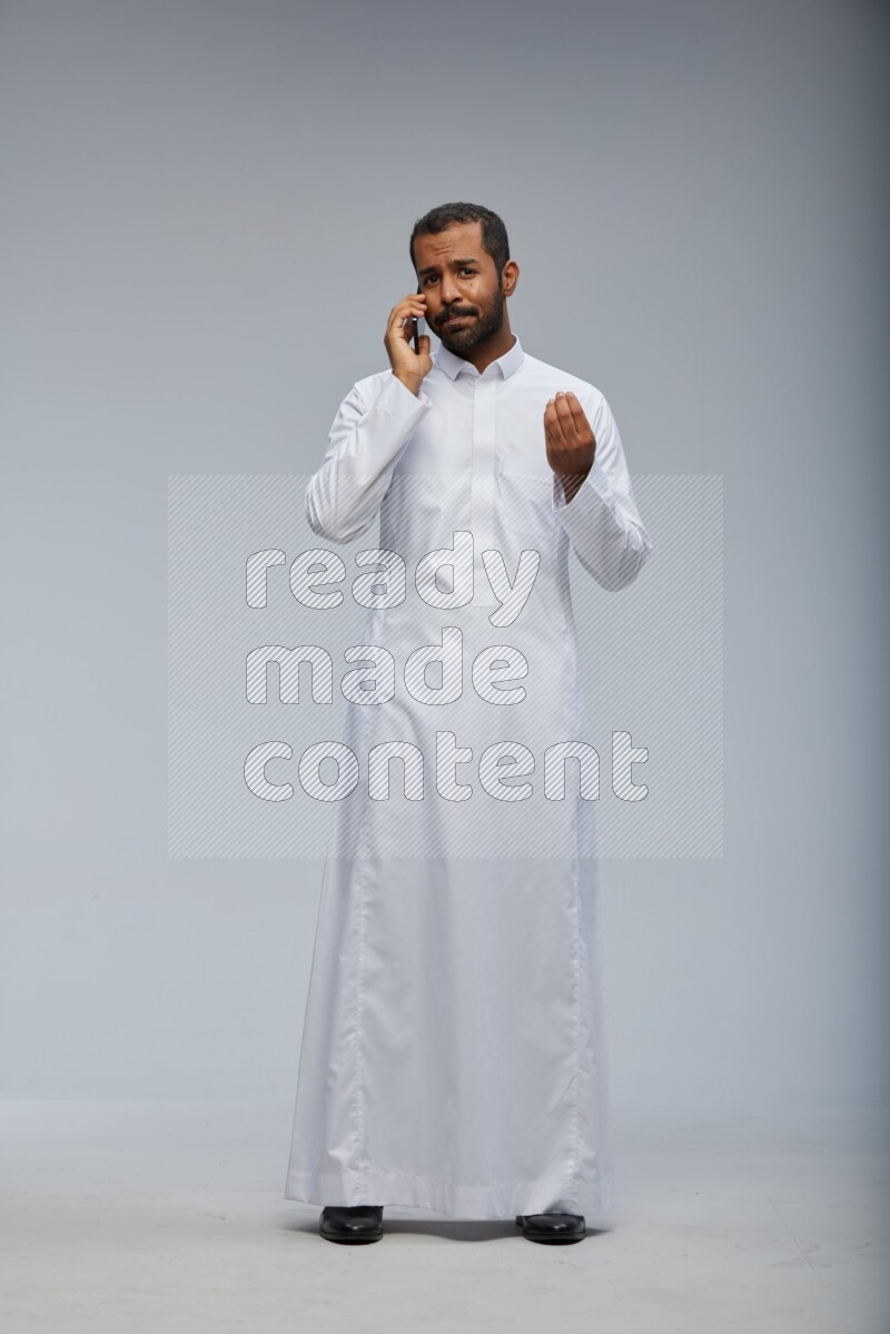 Saudi man wearing Thob standing talking on phone on Gray background