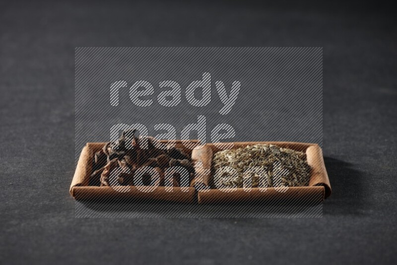 مربعان من أعواد القرفة ممتلئان بحبوب الكمون واليانسون النجمي علي خلفية سوداء