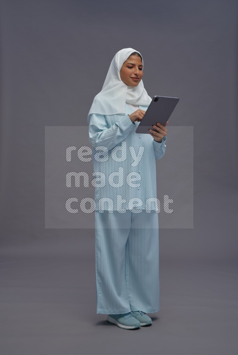 Saudi woman wearing hijab clothes standing working on tablet on gray background