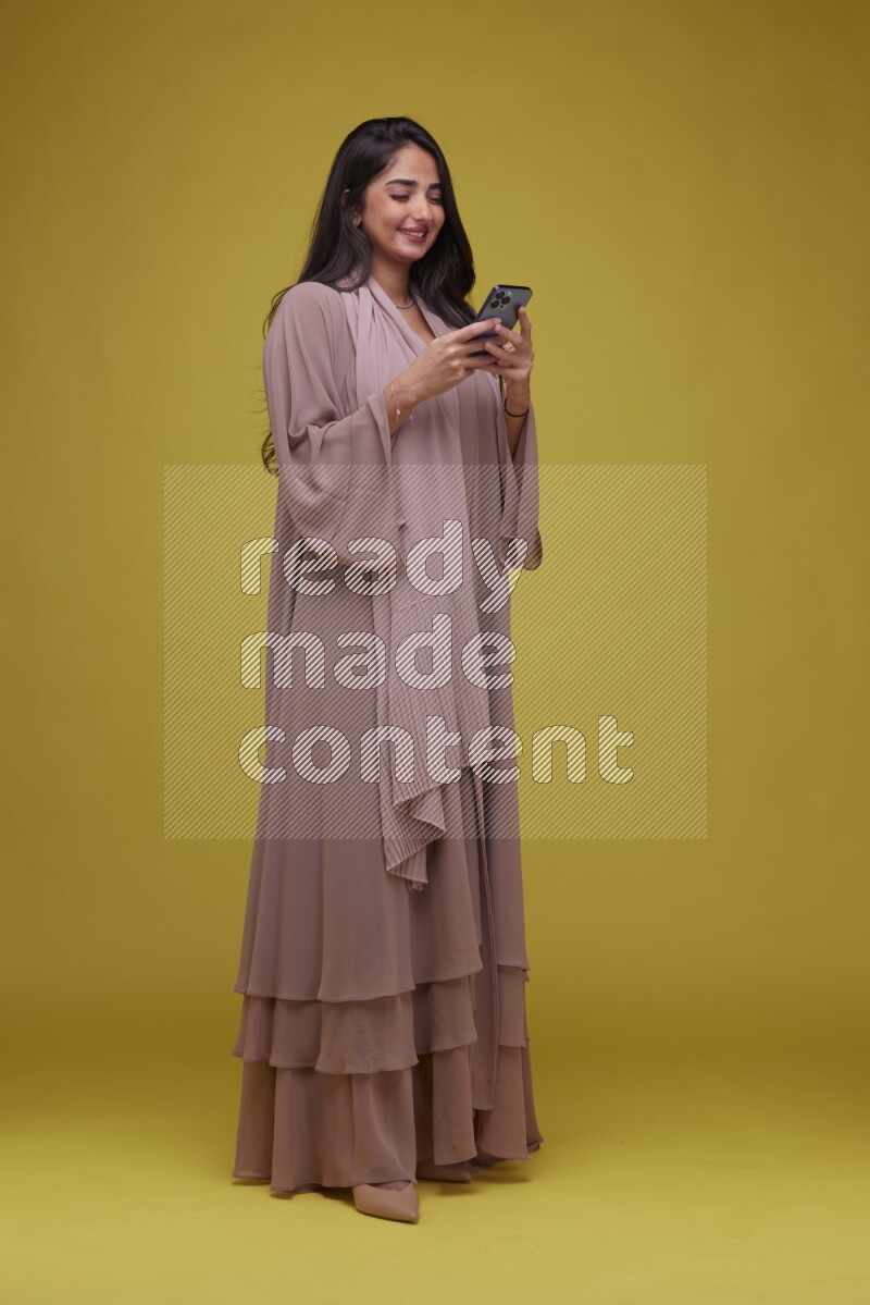 A woman Texting on a Yellow Background wearing Brown Abaya