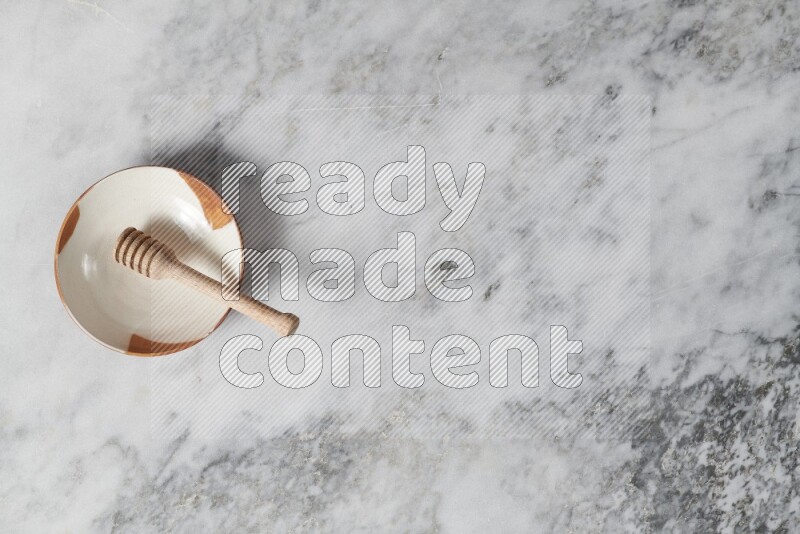 Multicolored pottery plate with wooden honey dipper in it on grey marble background