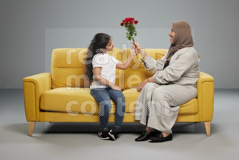 A girl sitting giving flowers to her mother on gray background