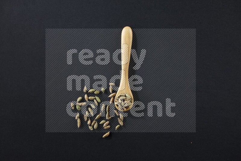 A wooden spoon full of cardamom on black flooring