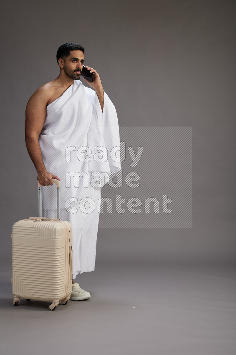 A man wearing Ehram Standing holding traveling bag on gray background
