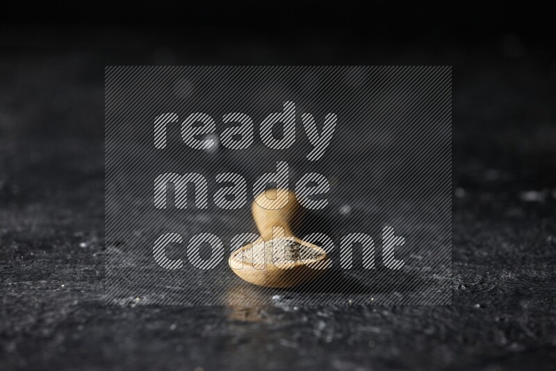 A wooden spoon full of white pepper powder on textured black flooring