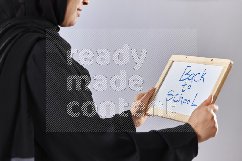 A woman in abaya holding books and a board in different positions (back to school)