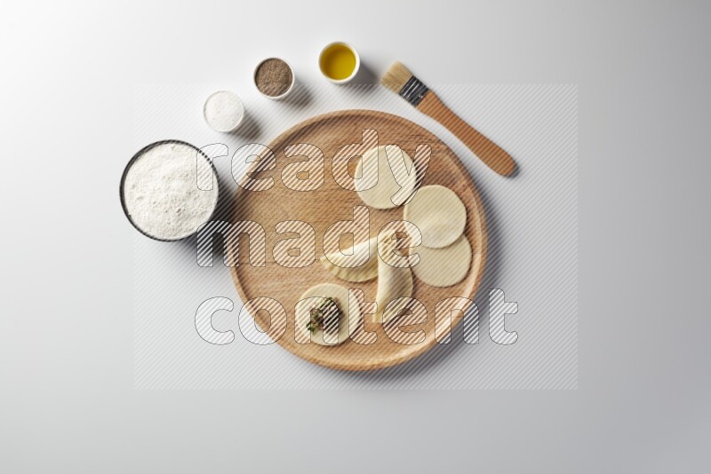 two closed sambosas and one open sambosa filled with meat while flour, salt, black pepper and oil with oil brush aside in a wooden dish on a white background
