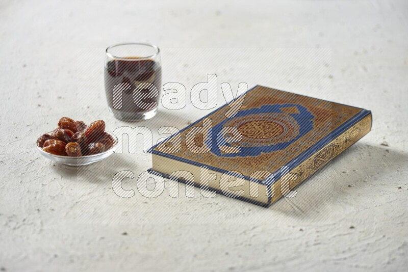 Quran with dates, prayer beads and different drinks all placed on textured white background