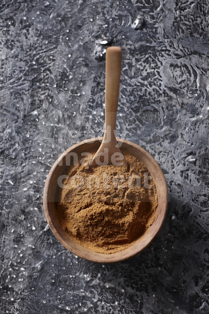 Wooden bowl full of cinnamon powder with a wooden spoon on a textured black background in different angles