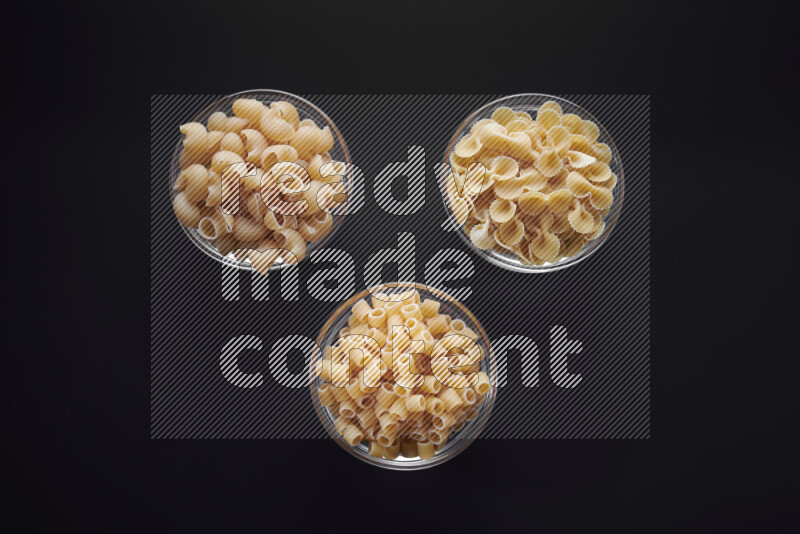 Different pasta types in glass bowls on black background