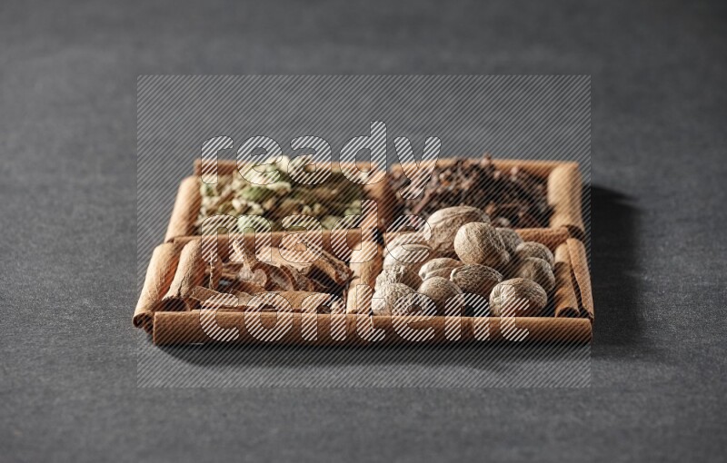 4 squares of cinnamon sticks full of cinnamon, cardamom, cloves and nutmegs on black flooring