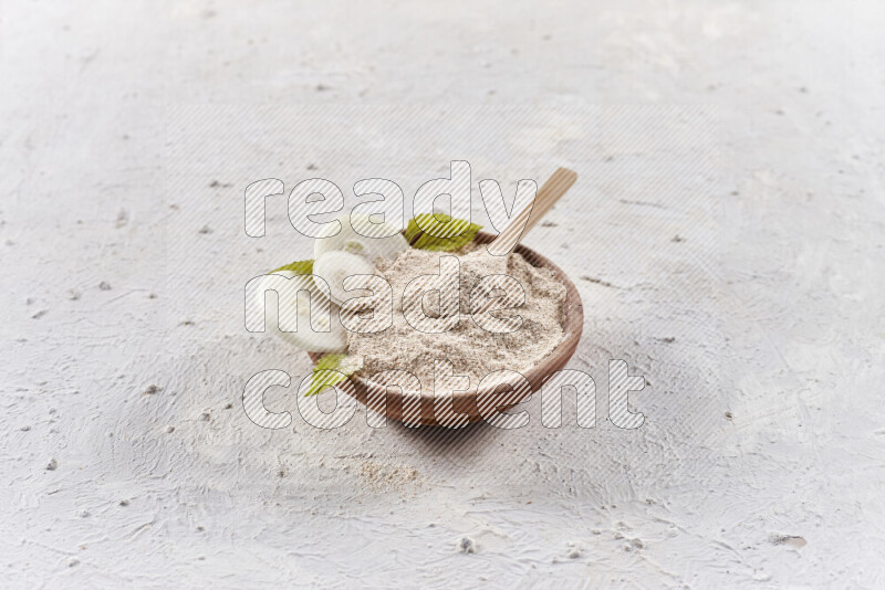 A wooden bowl full of onion powder with a wooden spoon in it with some sliced onions on white background