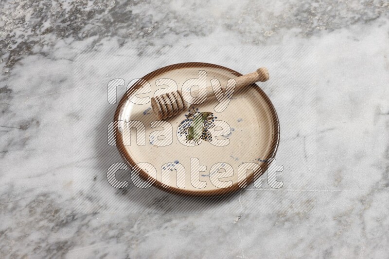 Decorative pottery plate with wooden honey dipper in it on grey marble background
