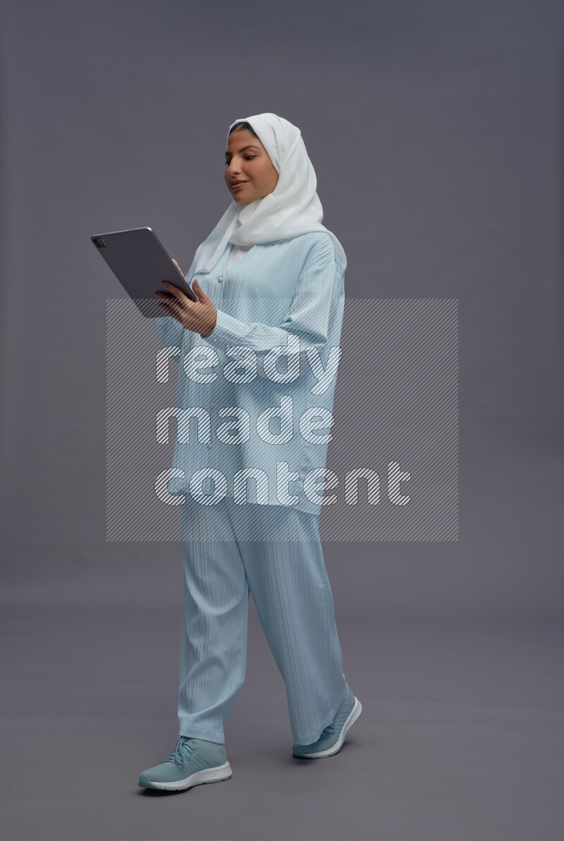 Saudi woman wearing hijab clothes standing working on tablet on gray background