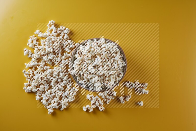 A brown pottery bowl full of popcorn with popcorn beside it on a yellow background in different angles
