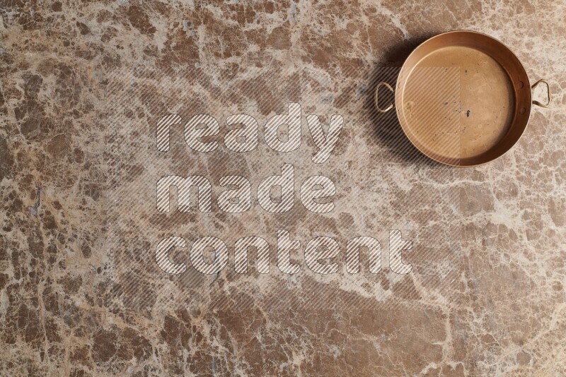 A small copper pan on beige marble background