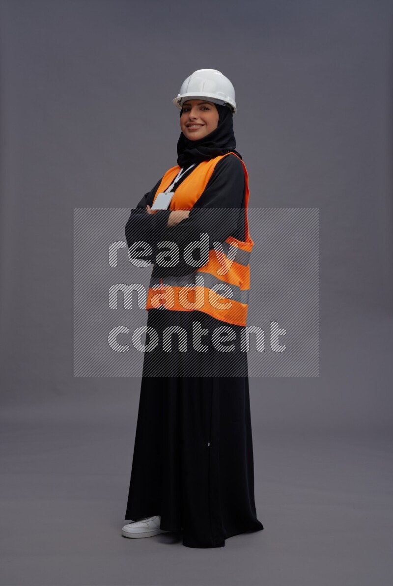 Saudi woman wearing Abaya with engineer vest with neck strap employee badge standing with crossed arms on gray background
