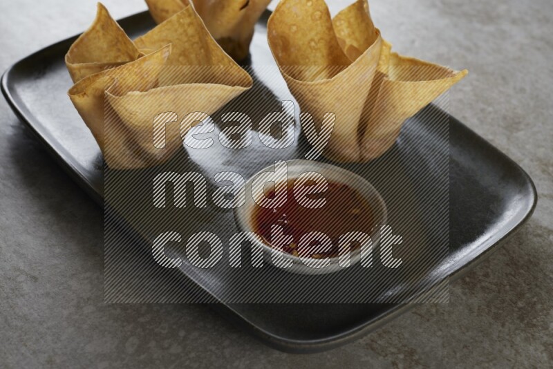wonton cups with soy sauce ramkin on rectangle dark grey ceramic plate on grey textured counter top