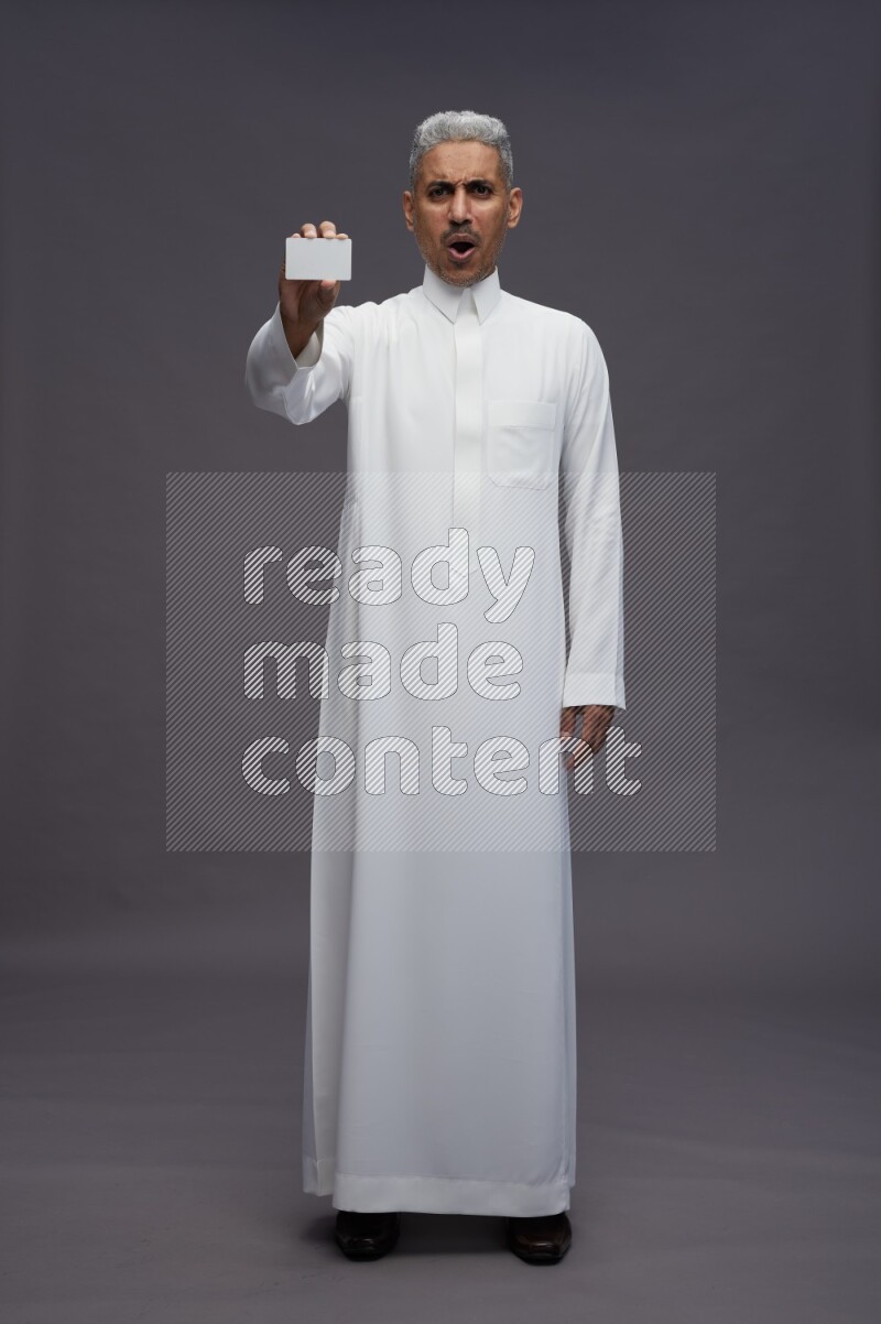 Saudi man wearing thob standing holding ATM card on gray background