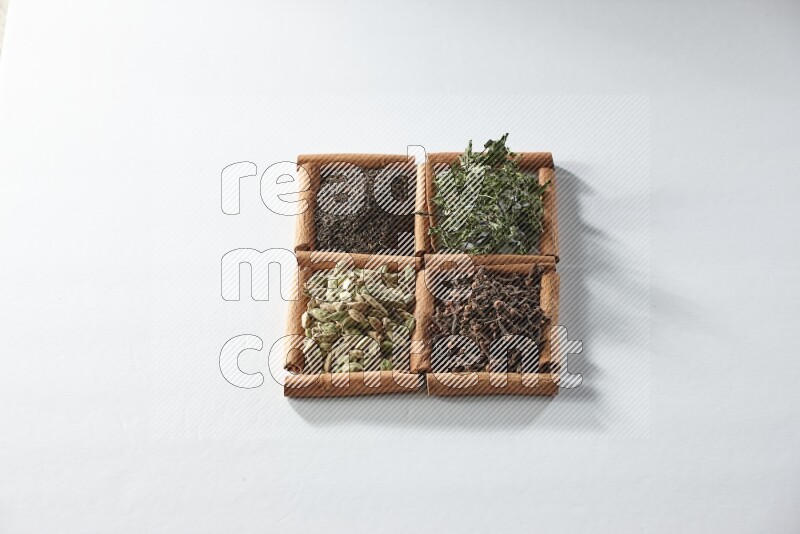 4 مربعات من أعواد القرفة ممتلئة بالشاي والهيل والنعناع والقرنفل على أرضية بيضاء