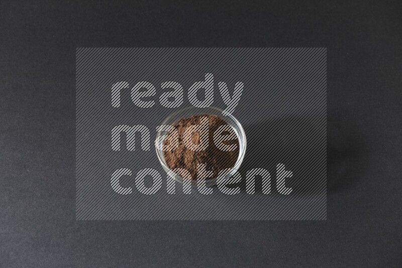 A glass bowl full of cloves powder on black flooring