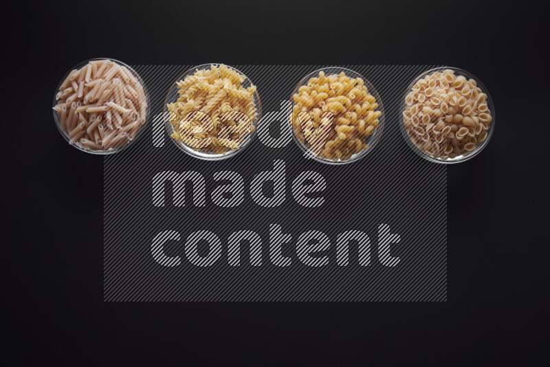 Different pasta types in glass bowls on black background