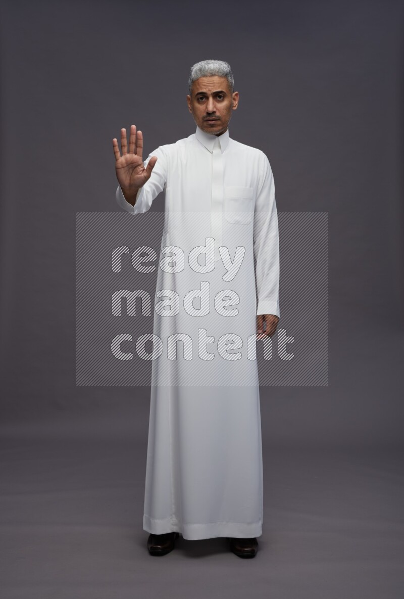 Saudi man wearing thob standing interacting with the camera on gray background