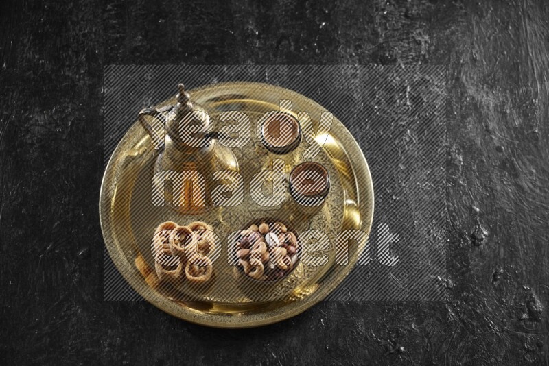 Oriental sweets with nuts and a drink on a metal tray in a dark setup