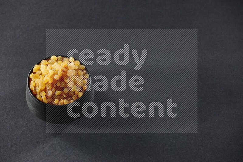 وعاء فخاري أسود ممتلئ بالزبيب الأصفر على خلفية سوداء