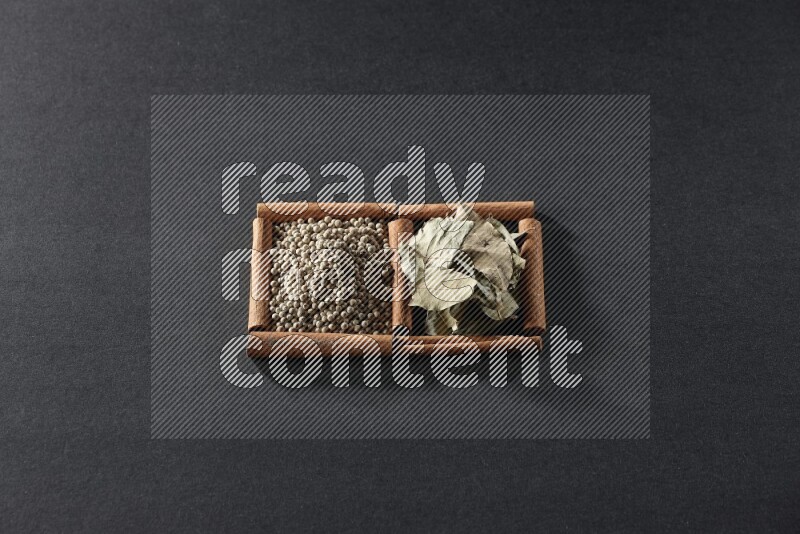 مربعان من أعواد القرفة ممتلئان بحبوب الفلفل الأبيض وأوراق الغار علي خلفية سوداء