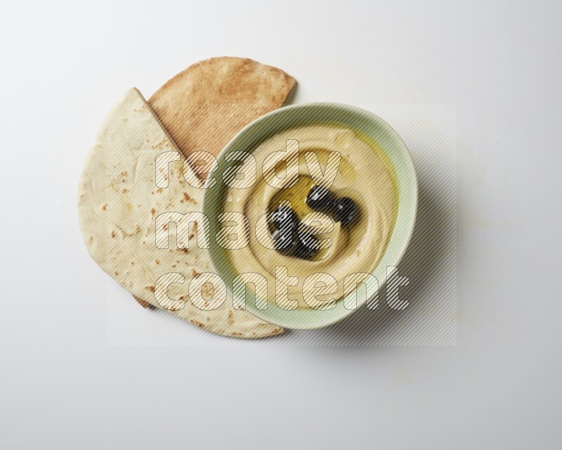Hummus in a green plate garnished with black olives on a white background