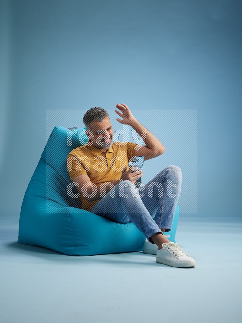 A man sitting on a blue beanbag and texting on phone
