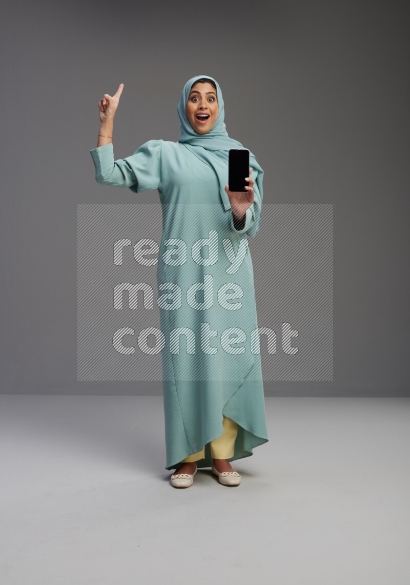 Saudi Woman wearing Abaya standing showing phone to camera on Gray background