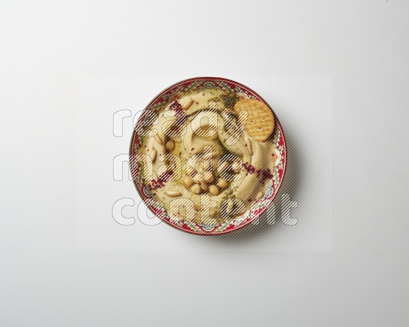 Hummus in a red plate with patterns garnished with zaatar & sumak on a white background