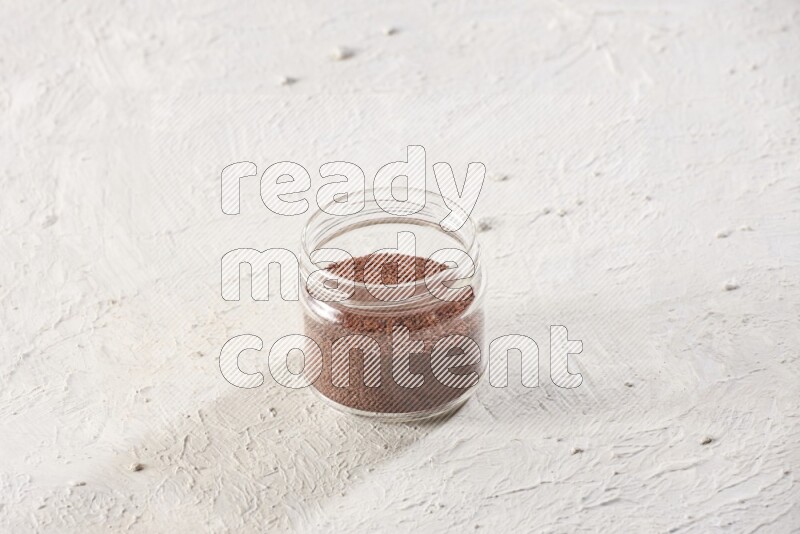 A glass jar full of garden cress seeds on a textured white flooring