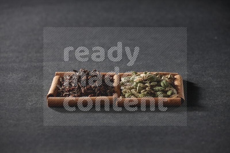 مربعان من أعواد القرفة ممتلئان بحبوب الهيل والقرنفل علي خلفية سوداء