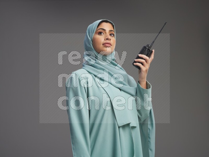 Saudi Woman wearing Abaya standing holding walkie-talkie on Gray background