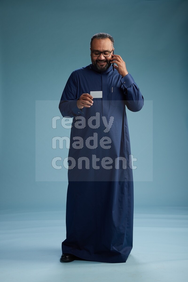 Saudi Man without shimag Standing holding ATM while talking on phone on blue background