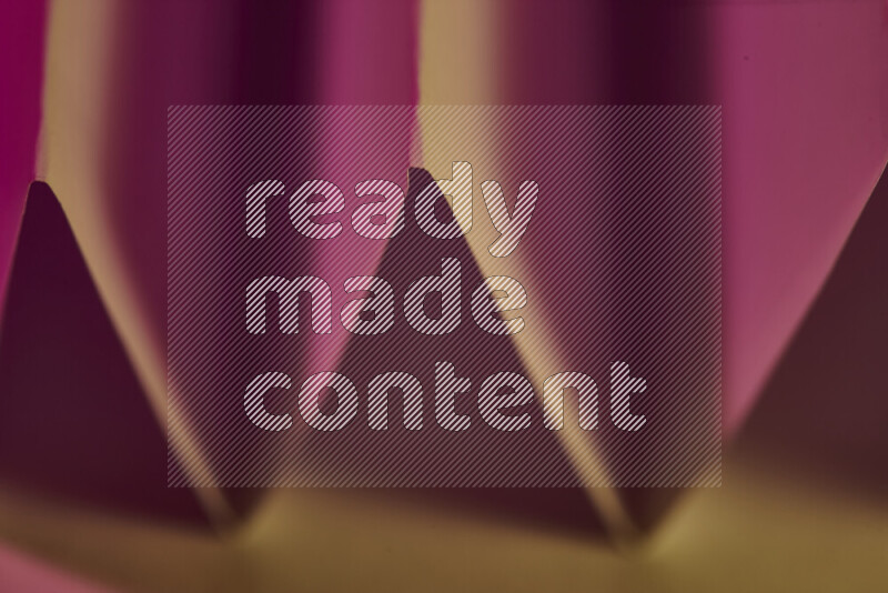 A close-up abstract image showing sharp geometric paper folds in pink gradients and warm tones
