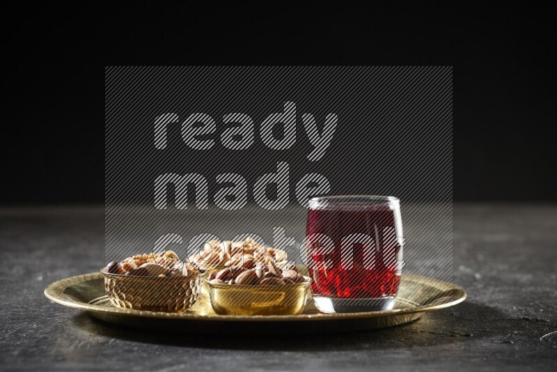 Nuts in metal bowls with Hibiscus on a tray in dark setup