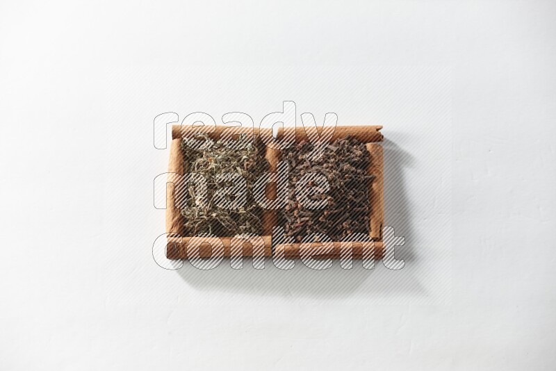 مربعان من أعواد القرفة ممتلئان بالقرنفل والريحان المجفف علي خلفية بيضاء