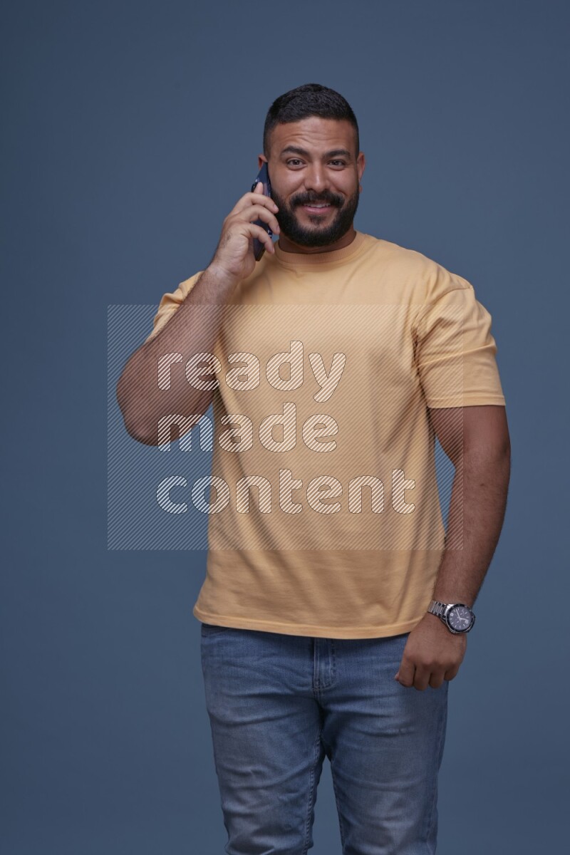 رجل يرتدي بنطال ازرق جينز وقميص اصفر بأكمام قصيره يتحدث بجواله