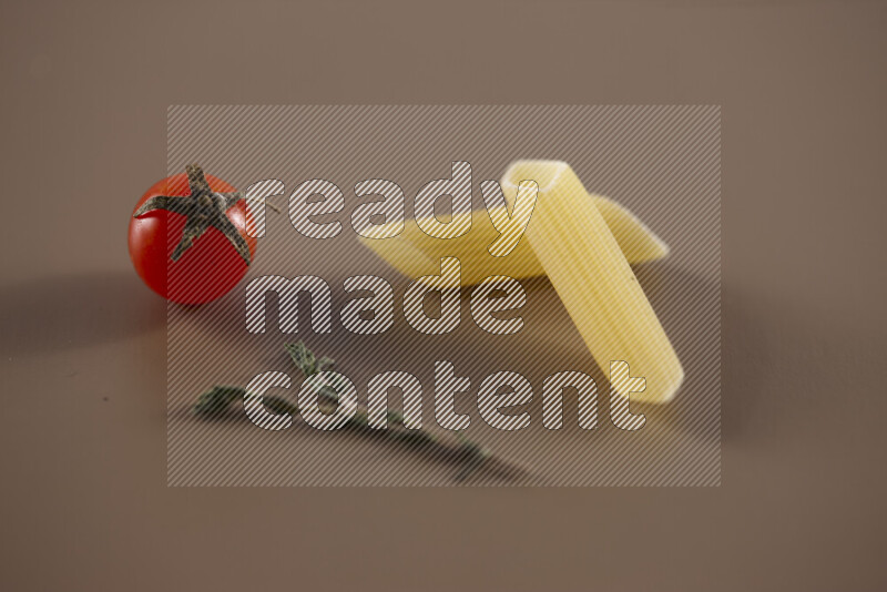 Raw pasta with different ingredients such as cherry tomatoes, garlic, onions, red chilis, black pepper, white pepper, bay laurel leaves, rosemary and cardamom on beige background