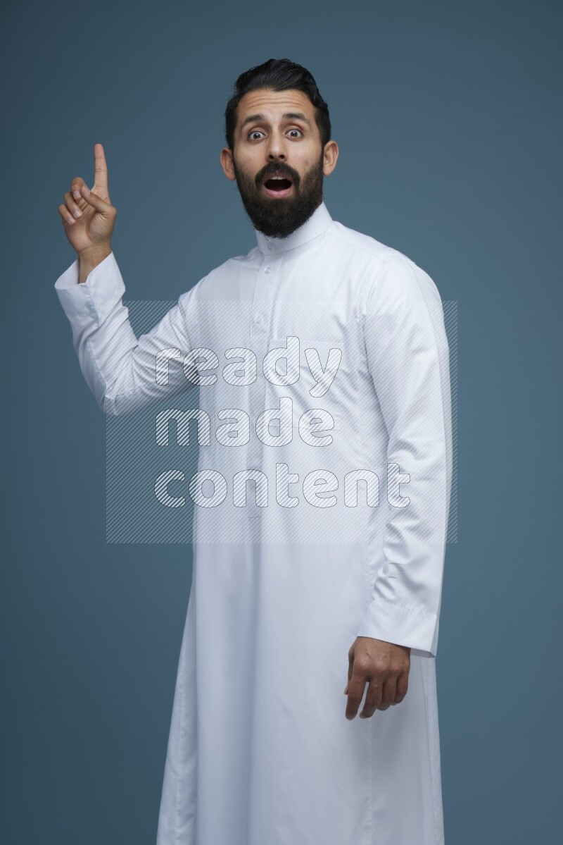 A man pointing in a blue background wearing Saudi Thob