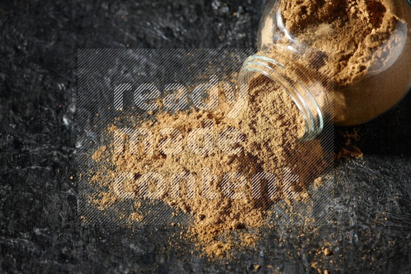 وعاء زجاجي للتوابل مقلوب ممتلئ ببودرة بهار الفلفل الحلو والبودرة تناثرت منه على خلفية سوداء