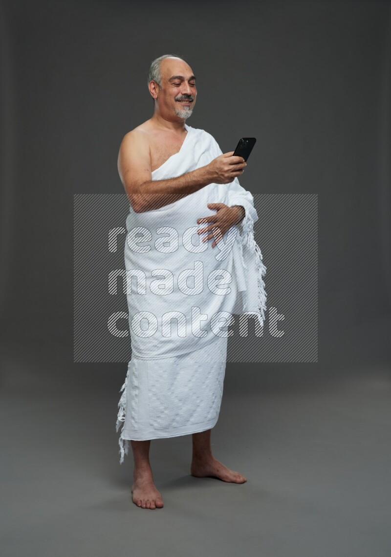 A man wearing Ehram Standing texting on phone on gray background