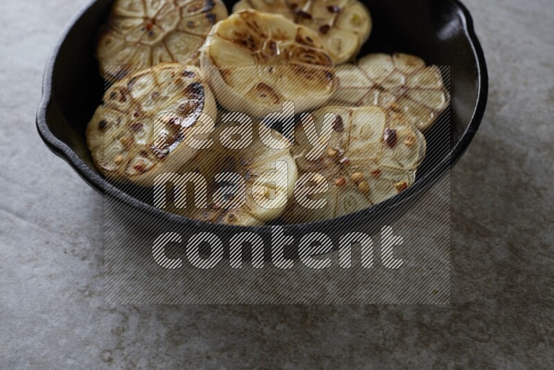 half's roasted garlic in a black pan on a grey textured countertop