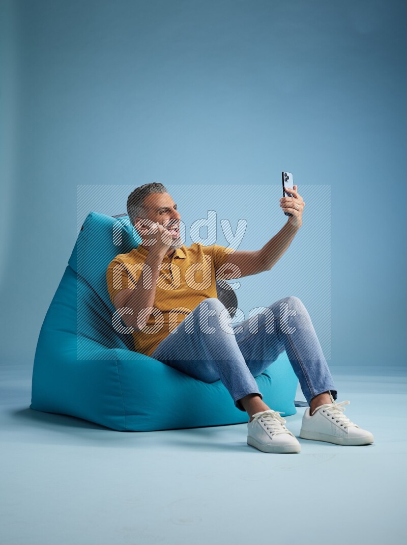 A man sitting on a blue beanbag and taking selfie
