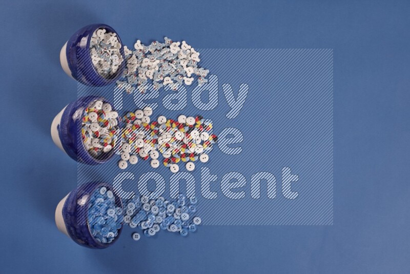 Multicolored pottery bowls full of colored buttons on blue background